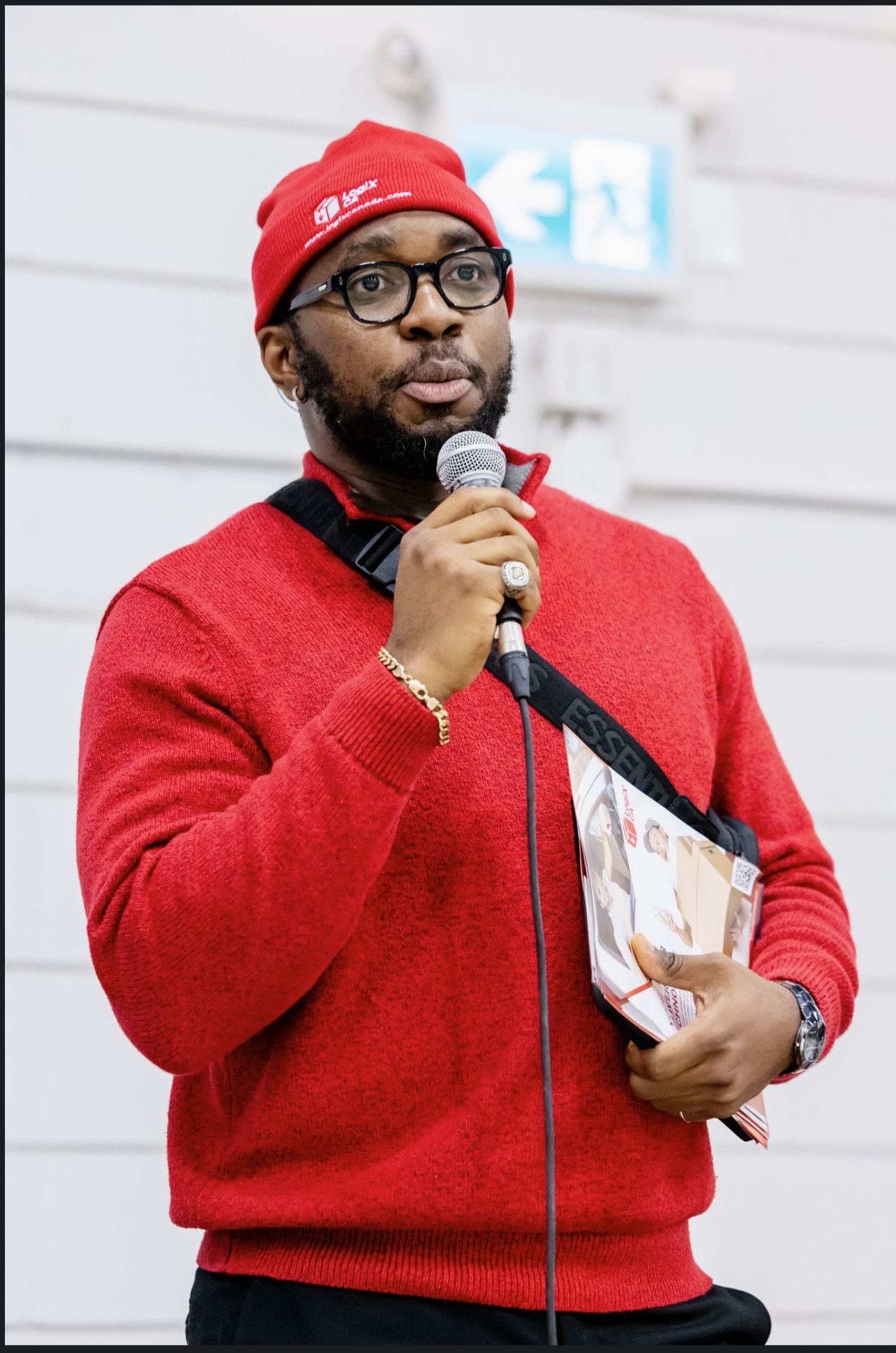 LogiX Canada team member in branded red beanie speaking on a microphone at the Caribbean Winter Food Festival in Edmonton